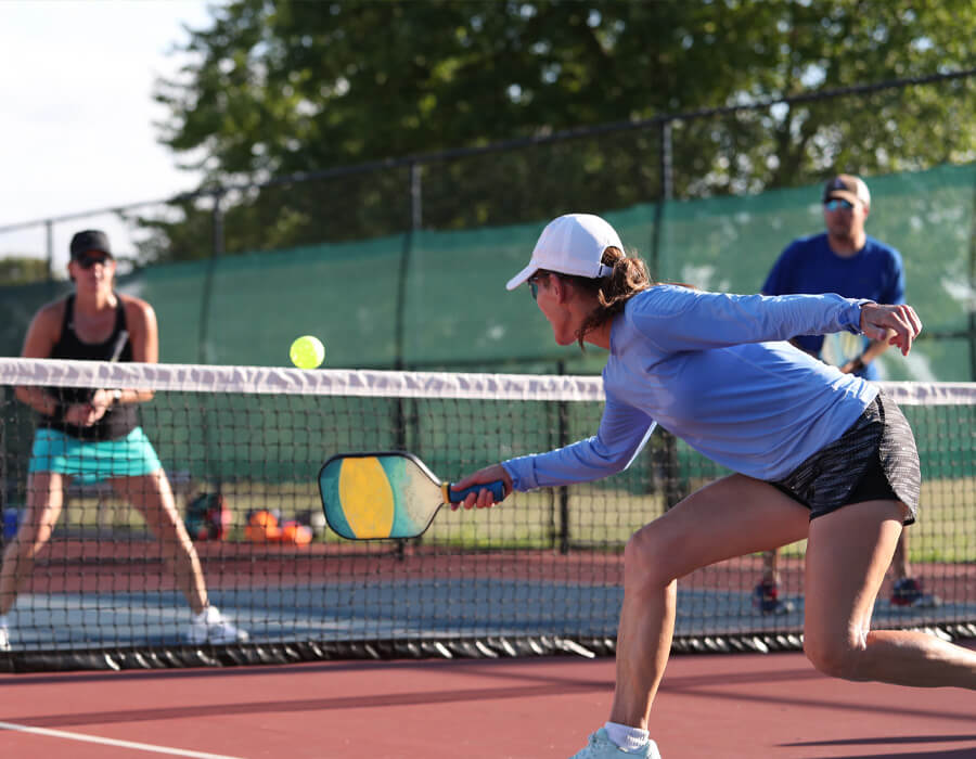 Players enjoying a game of pickleball on outdoor courts at Sand Dune Park with palm trees in the background.
