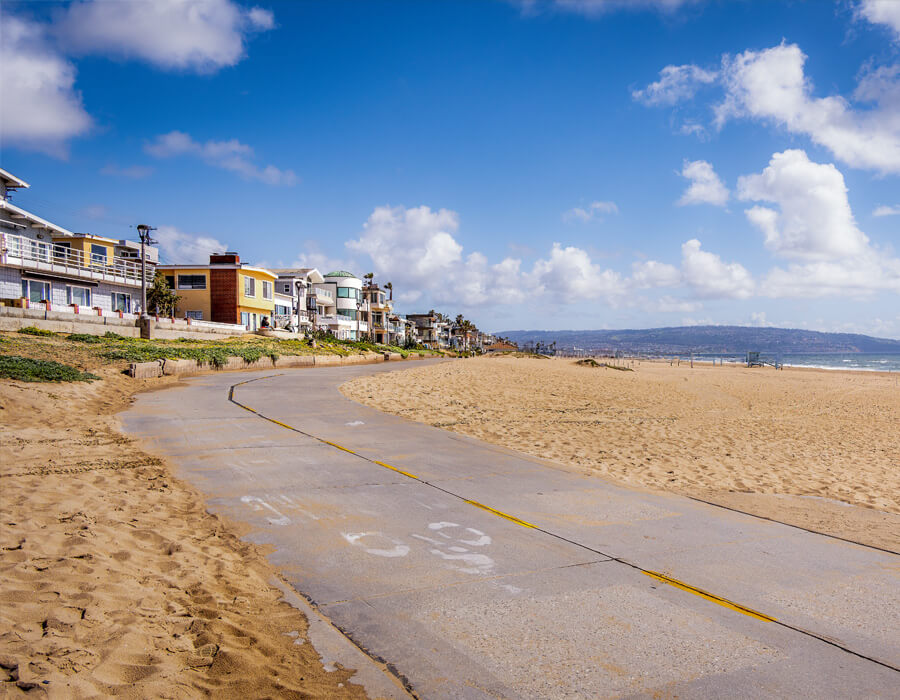 Scenic view of The Strand bike path along the ocean, lined with beach homes and palm trees.