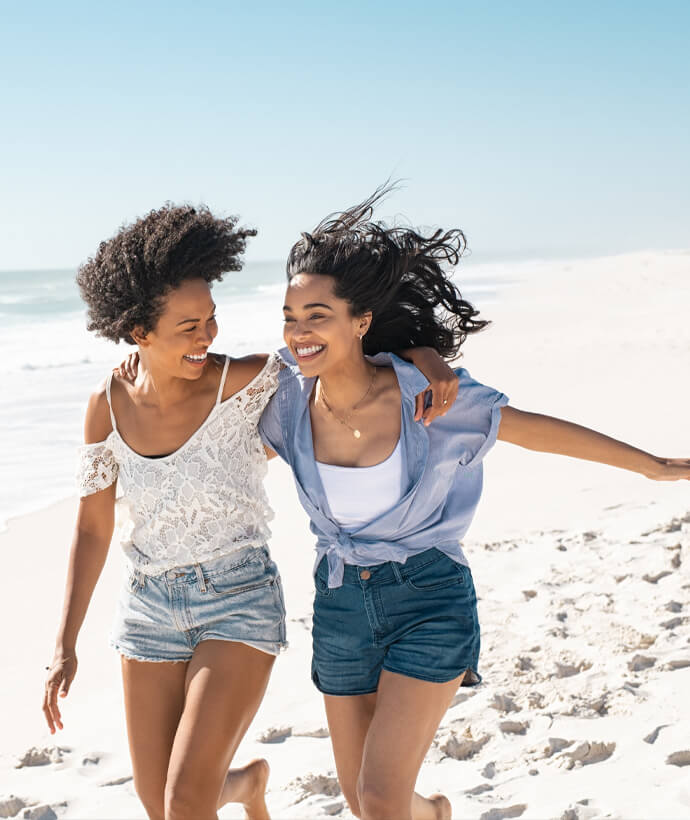 Two girls standing on the sandy beach, smiling and enjoying the ocean breeze at Manhattan Beach.